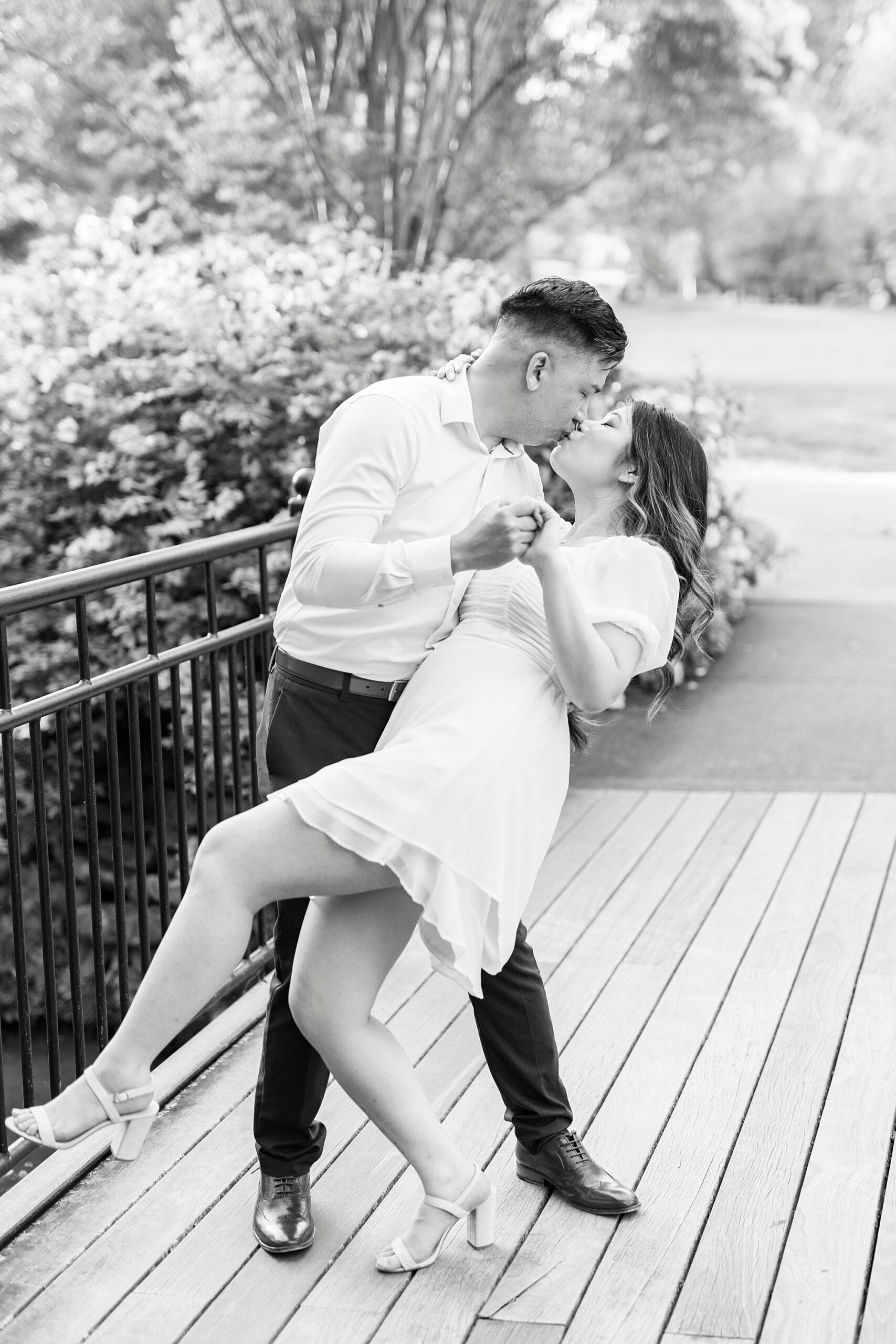 engaged couple kisses dipping on wooden bridge at Glencairn Garden