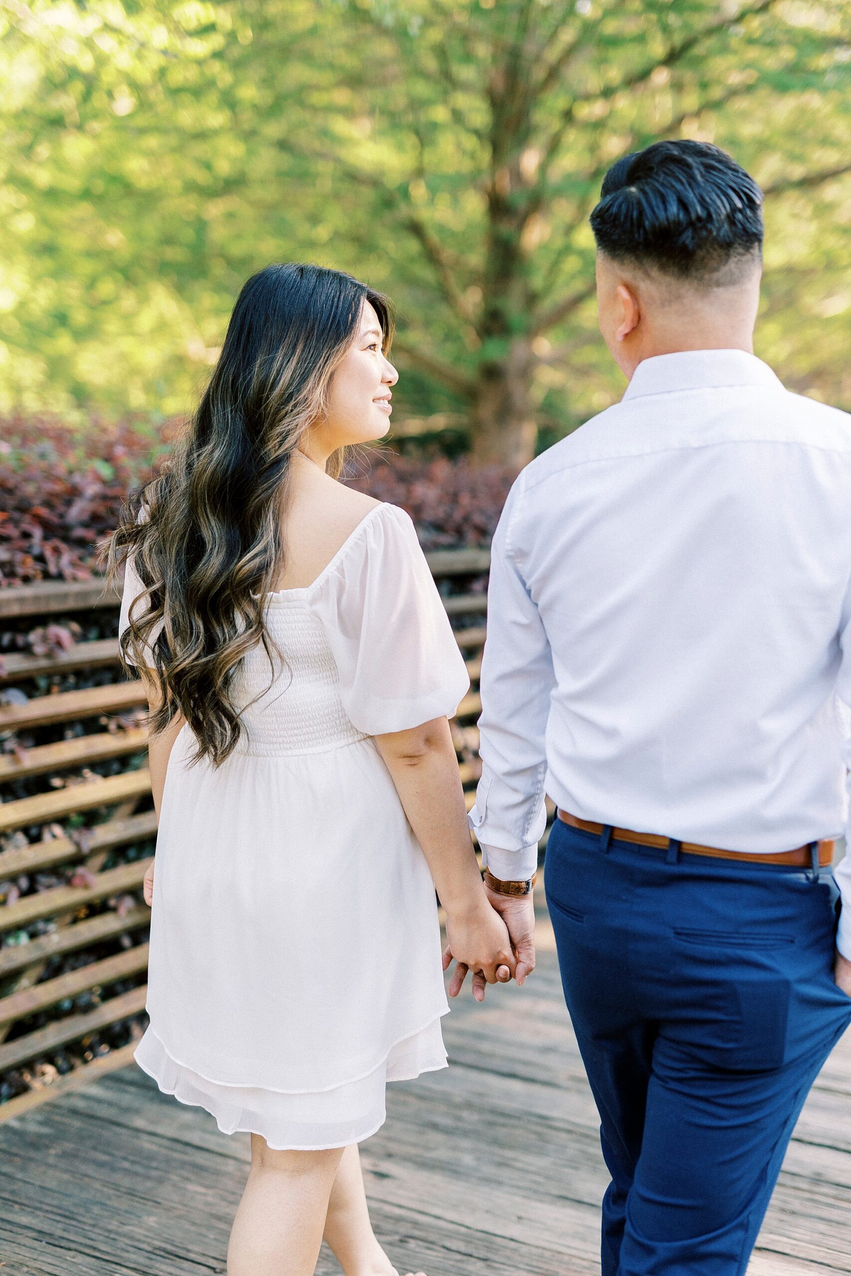 couple holds hands walking on the bridge at Glencairn Garden