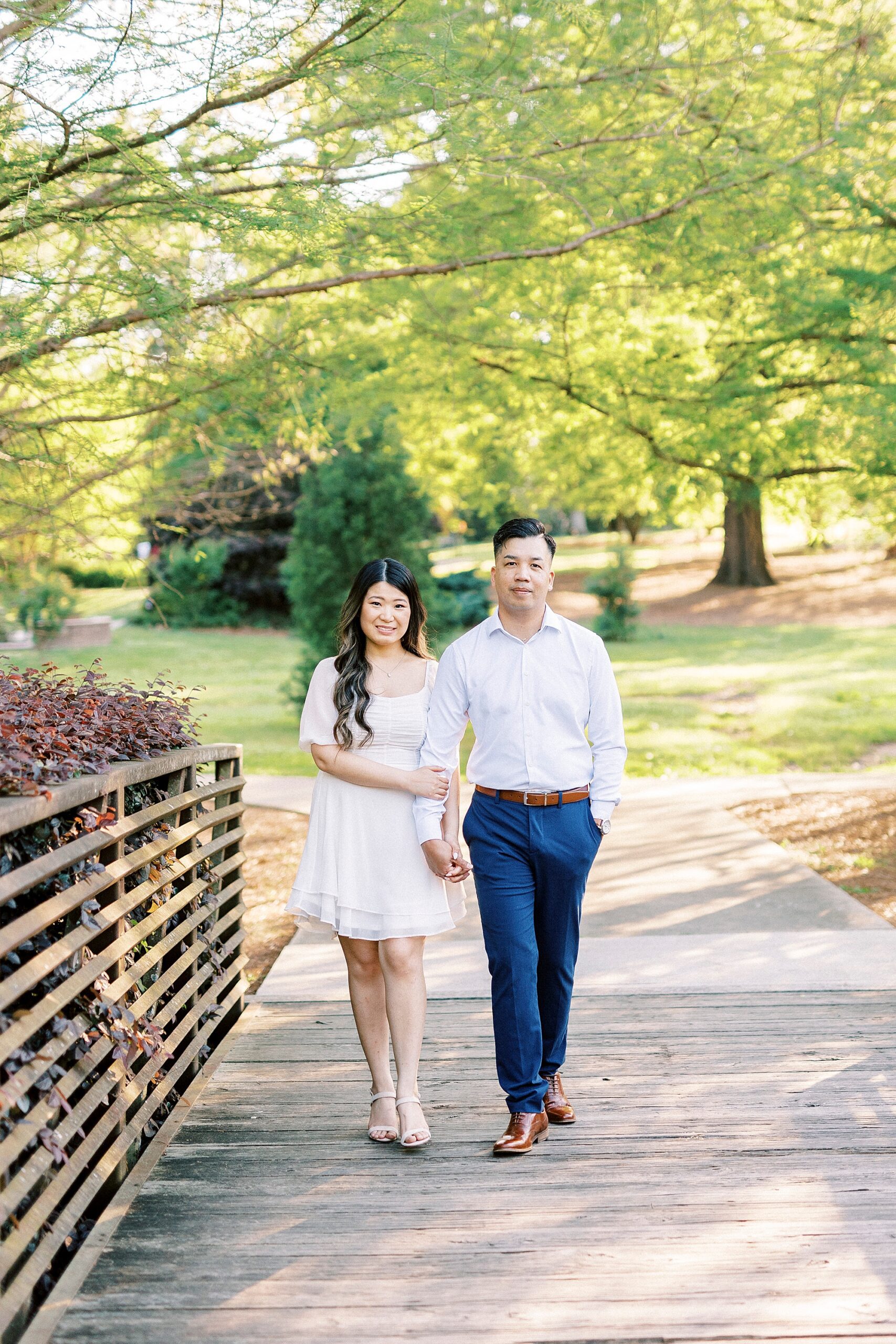 couple holds hands walking on bridge inside Glencairn Garden