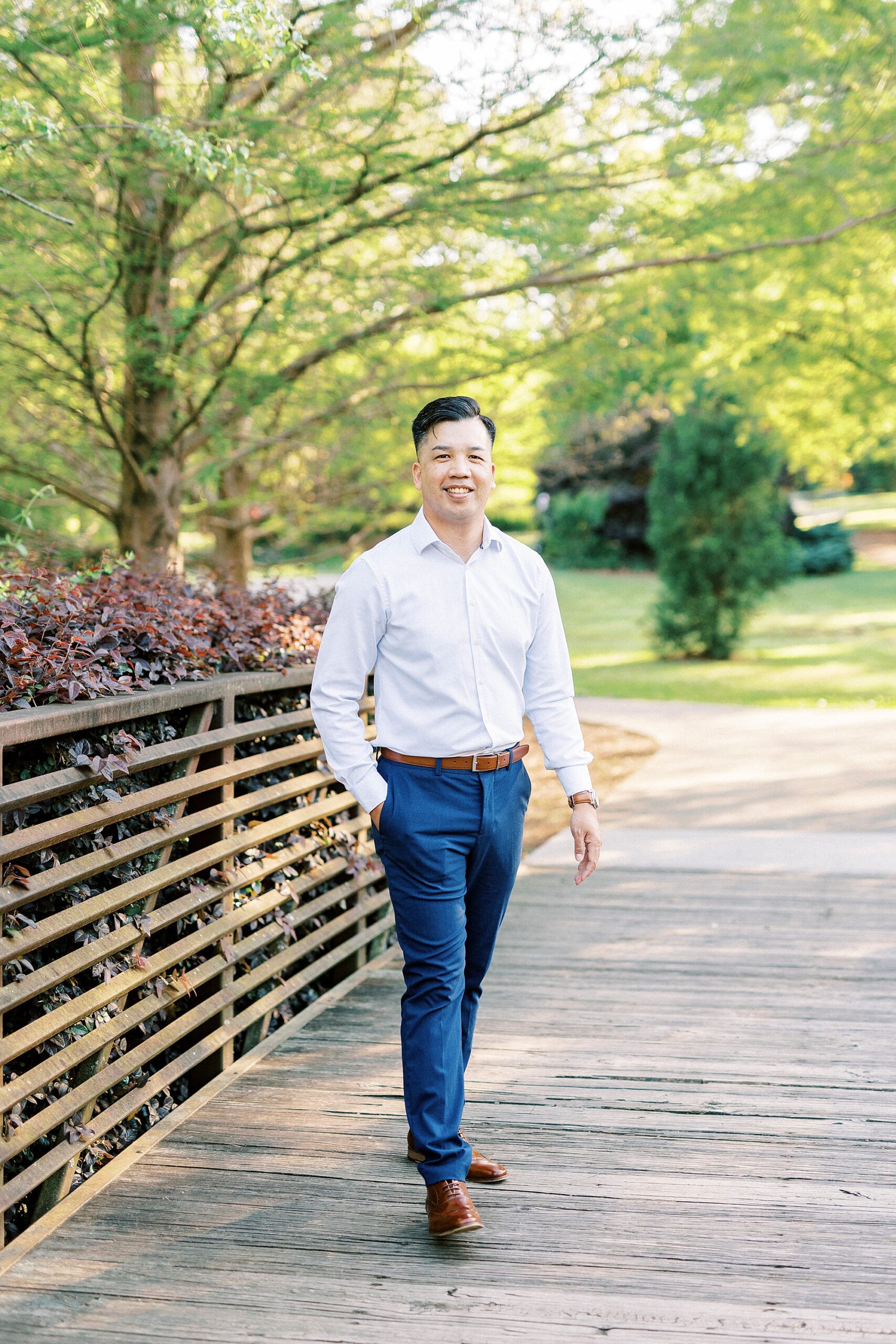 man in blue button down and blue pants stands on wooden bridge