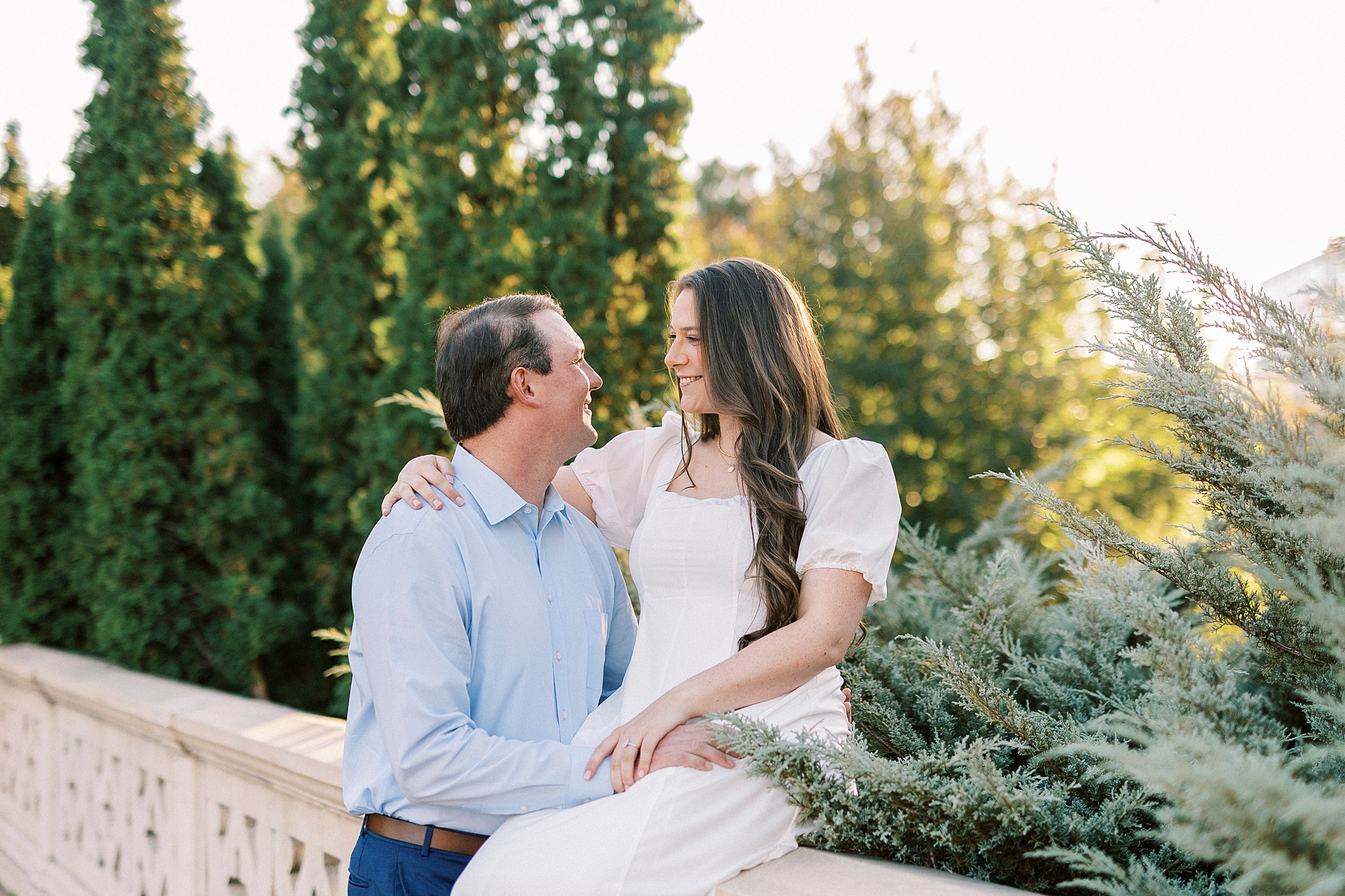 man stands by fiancee sitting on stone wall inside Midtown Park