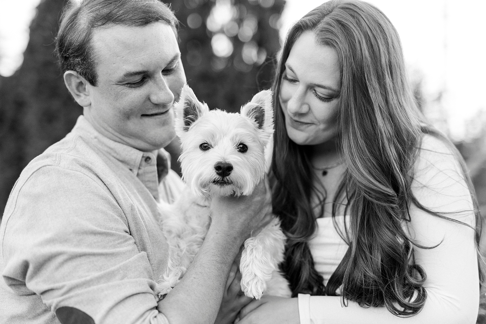 engaged couple stands holding dog between them during engagement photos