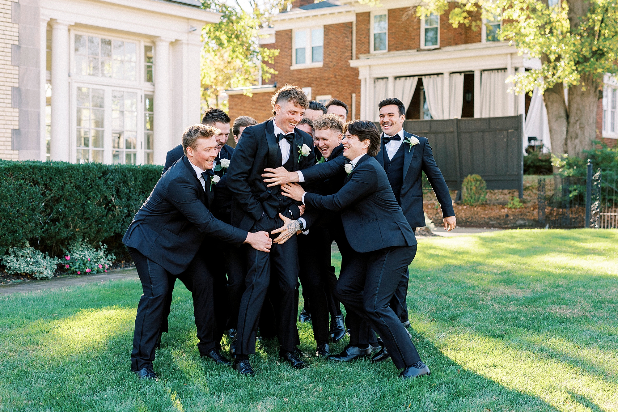 groomsmen lift up groom on lawn at Separk Mansion