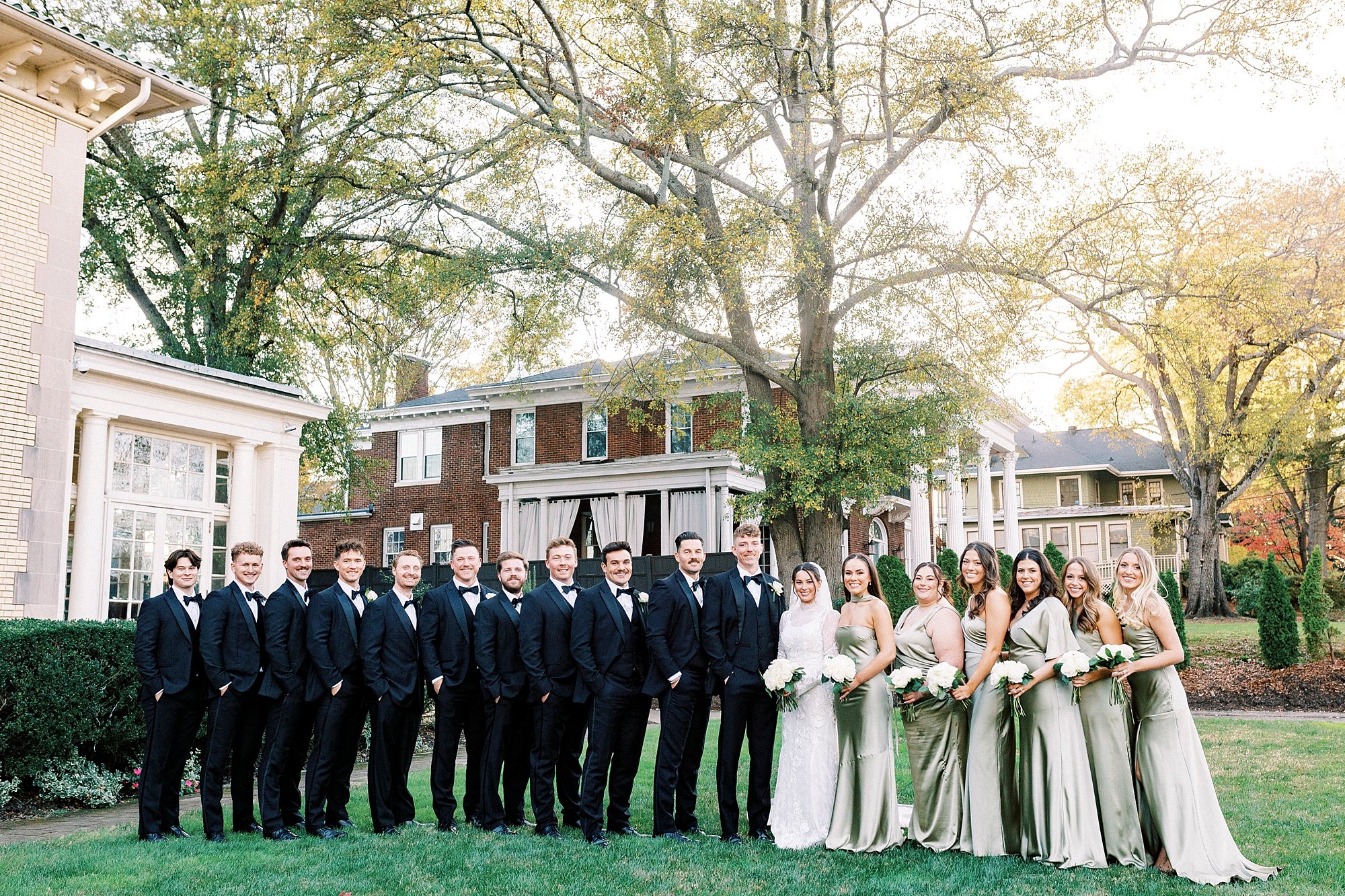 bride and groom stand on lawn at Separk Mansion with wedding party in sage green and black attire