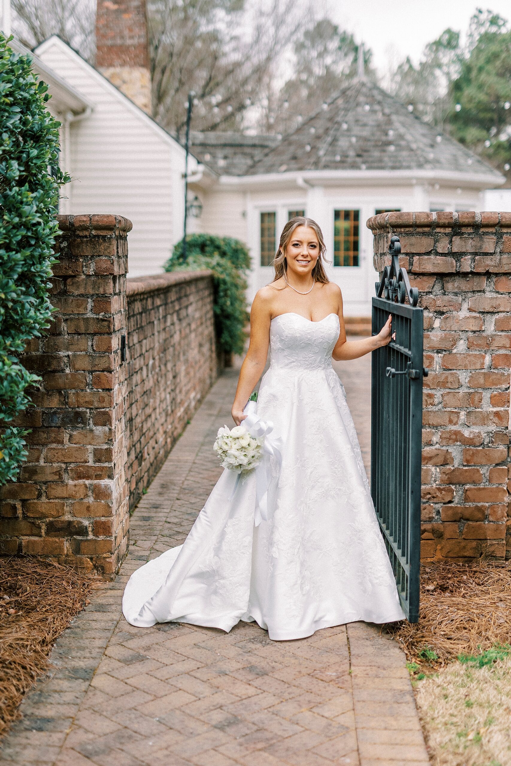 bride stands between opening of brick gate with wrought iron door