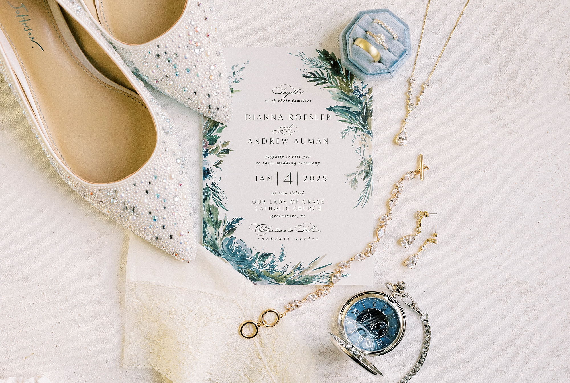 bride's shoes, rings, and invitation suite with green and blue floral accents for winter wedding