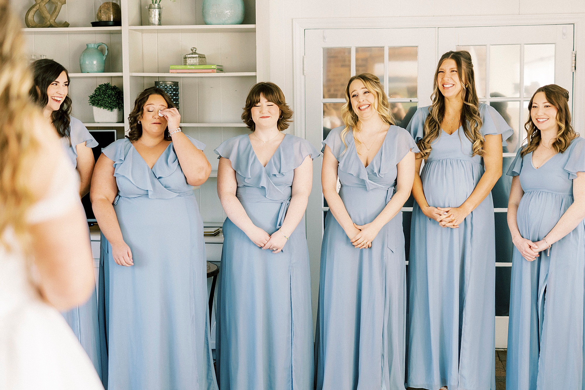 bridesmaids in blue dresses react to bride's look during first look