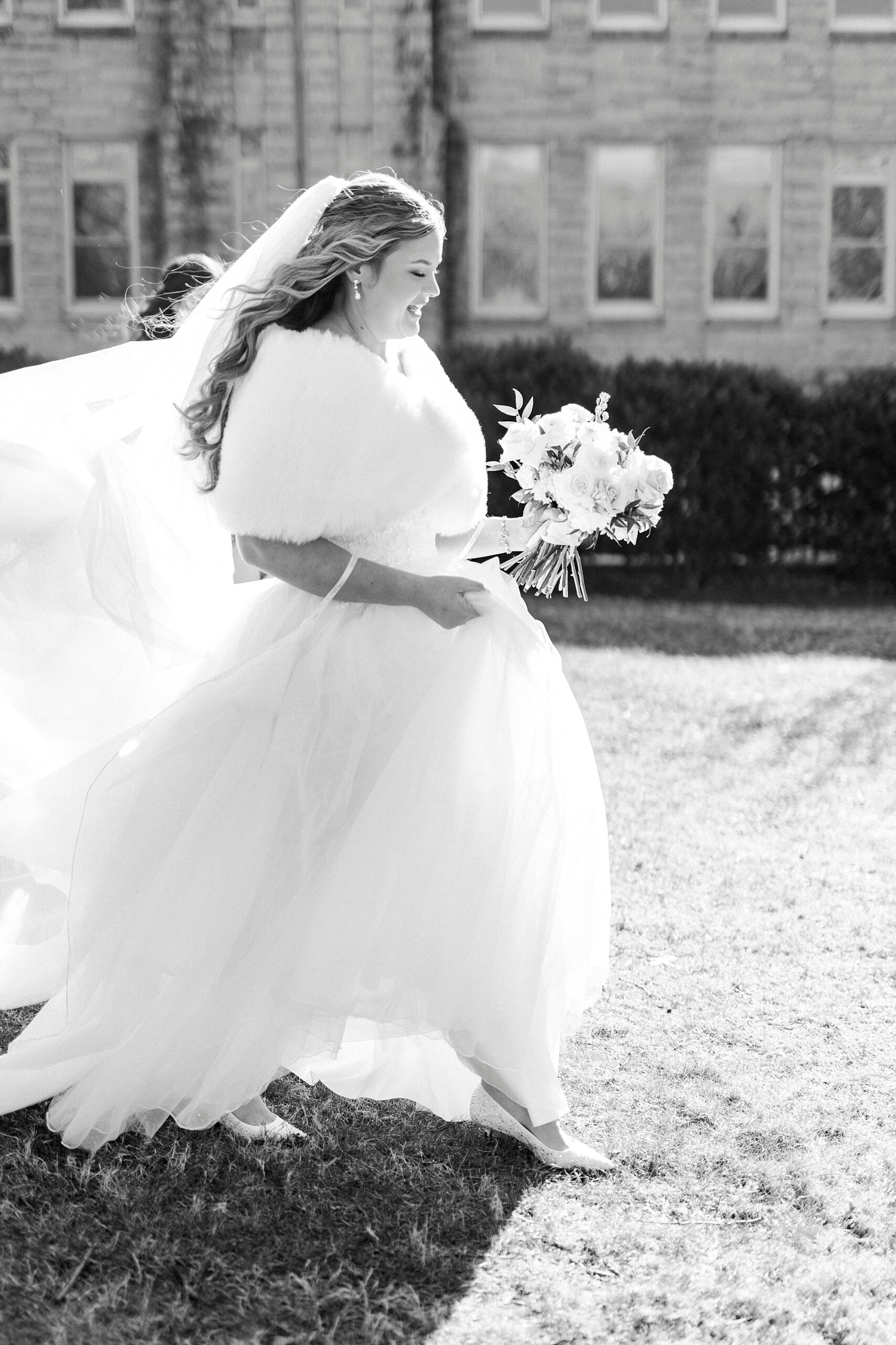 bride walks on lawn with fur and bouquet of flowers outside Our Lady of Grace