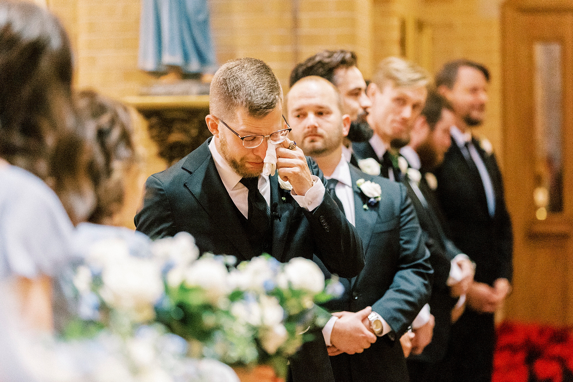 groom wipes away tears standing at alter during wedding ceremony at Our Lady of Grace