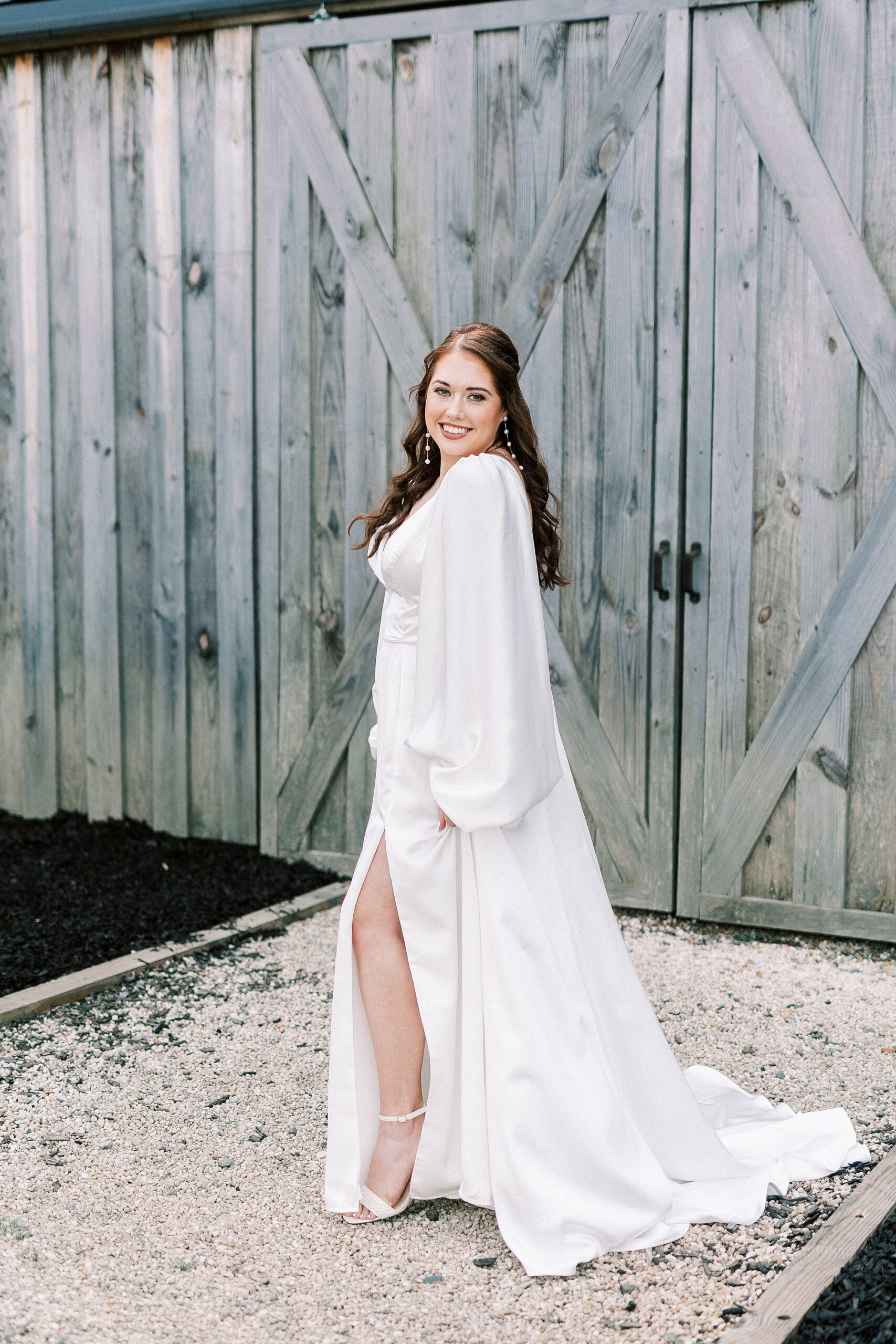 bride poses in front of worn wooden door in wedding gown showing off her leg