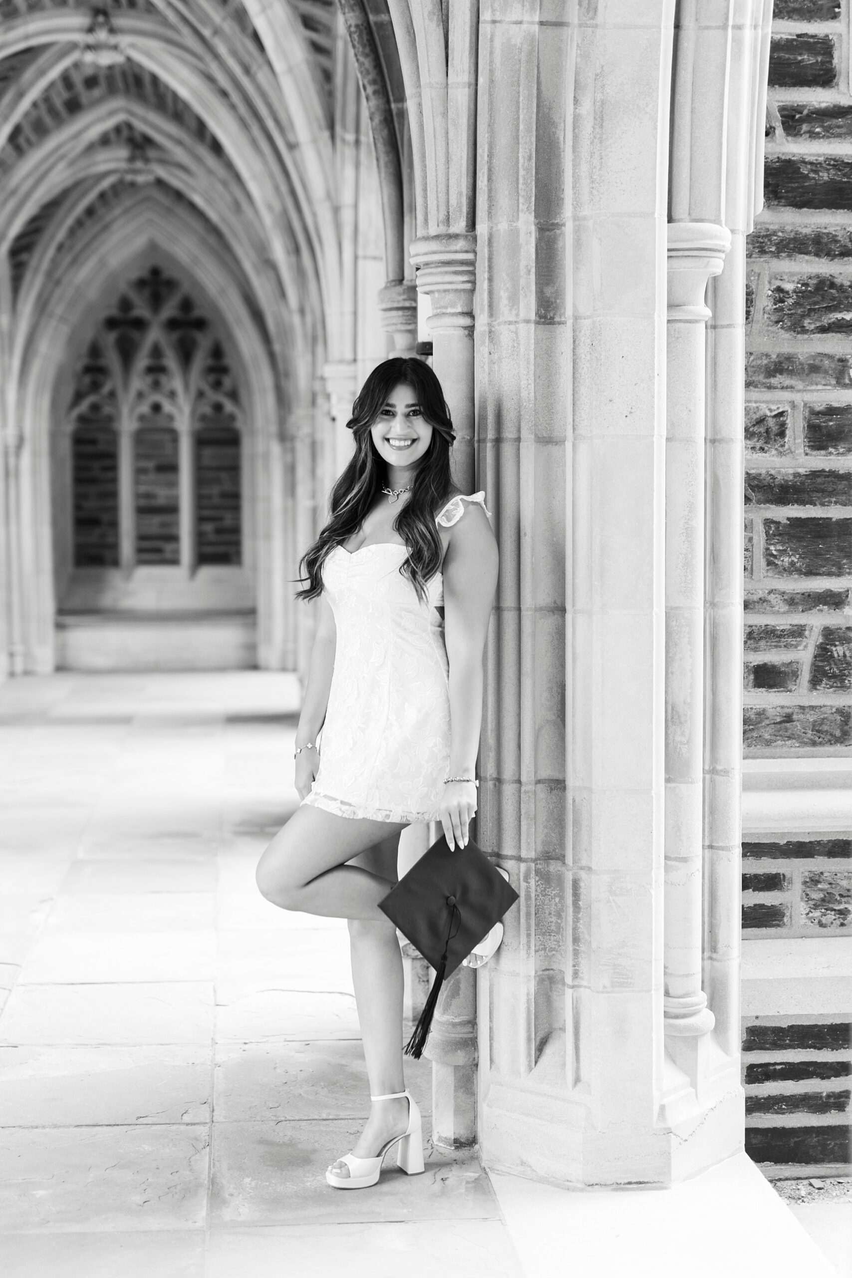 senior leans against archway at Duke Chapel holding graduation cap