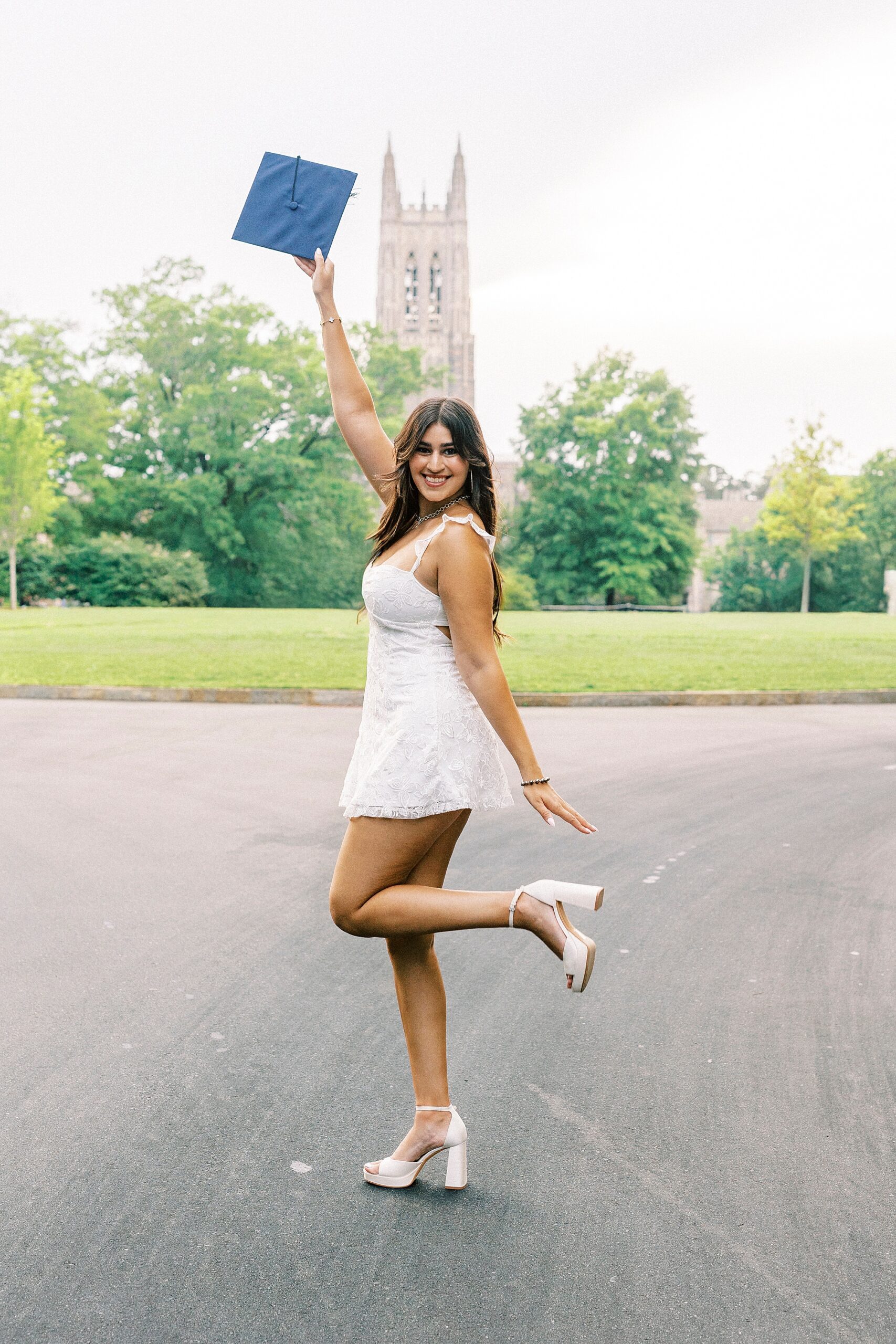 girl poses with blue graduation cap in front of bell tower at Duke University