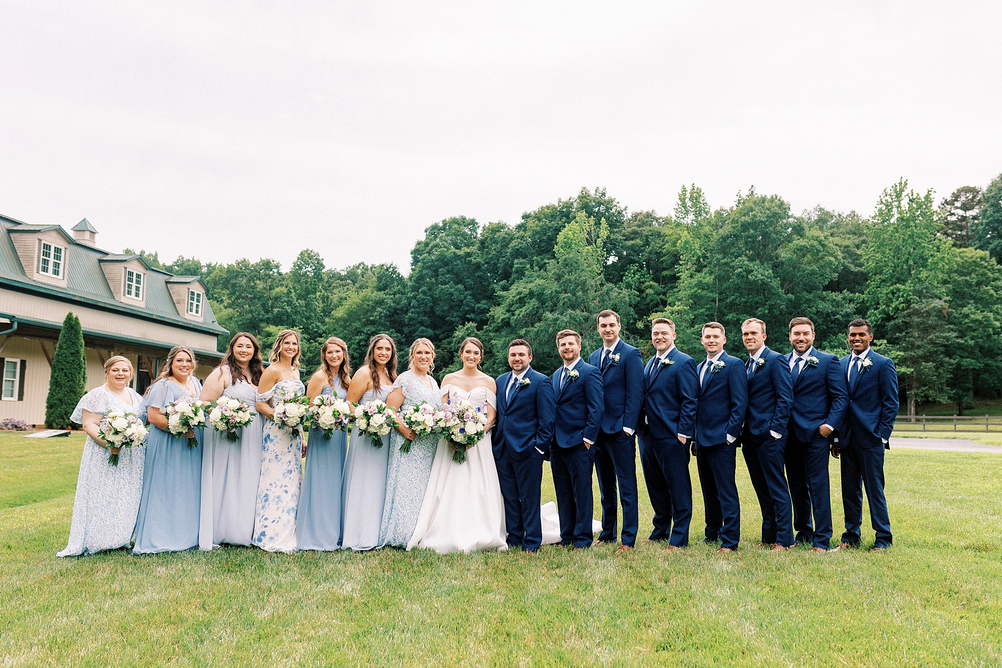 bride and groom stand with wedding party in light blue dresses and blue suits