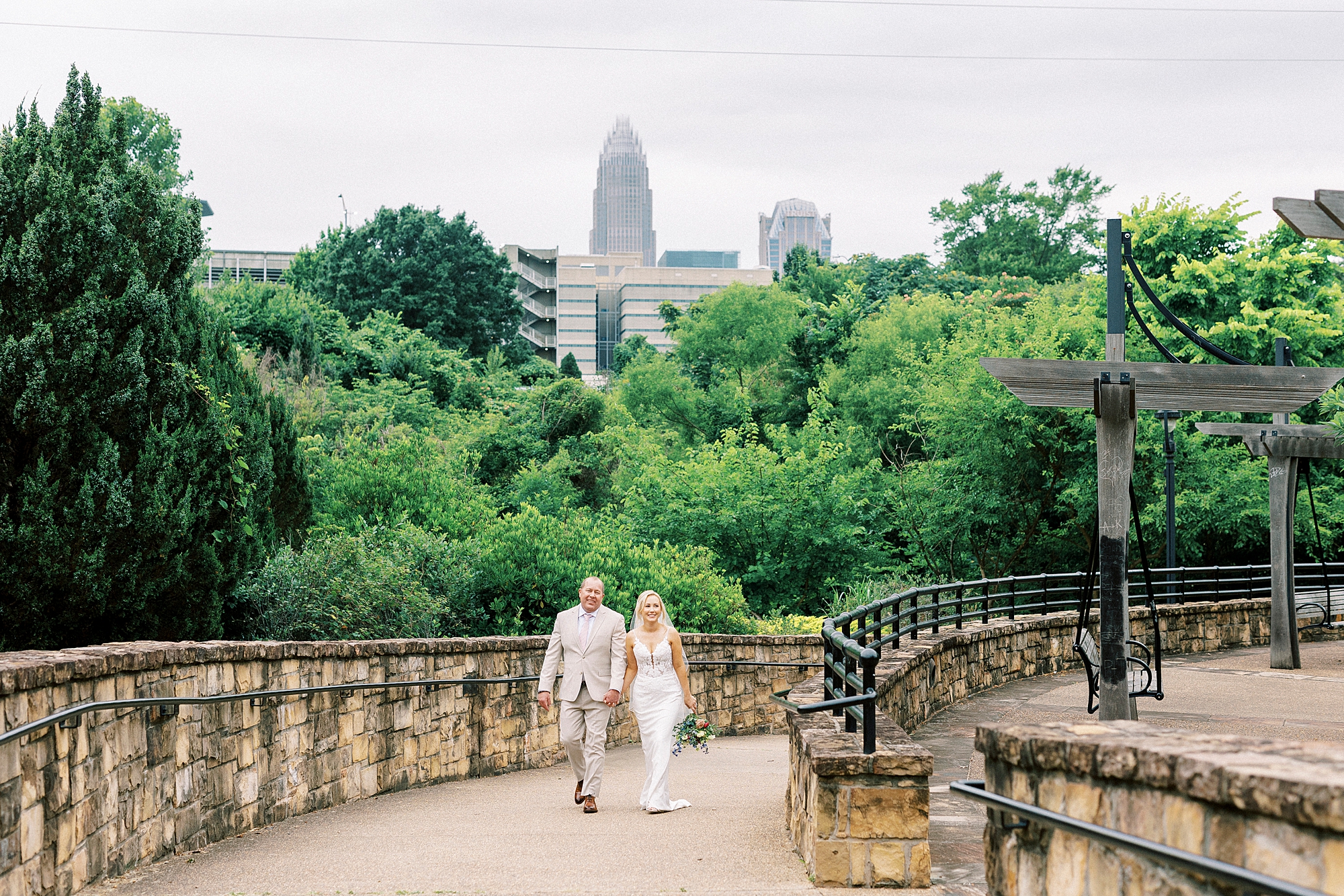 bride and groom hold hands walking thorough Uptown Charlotte park