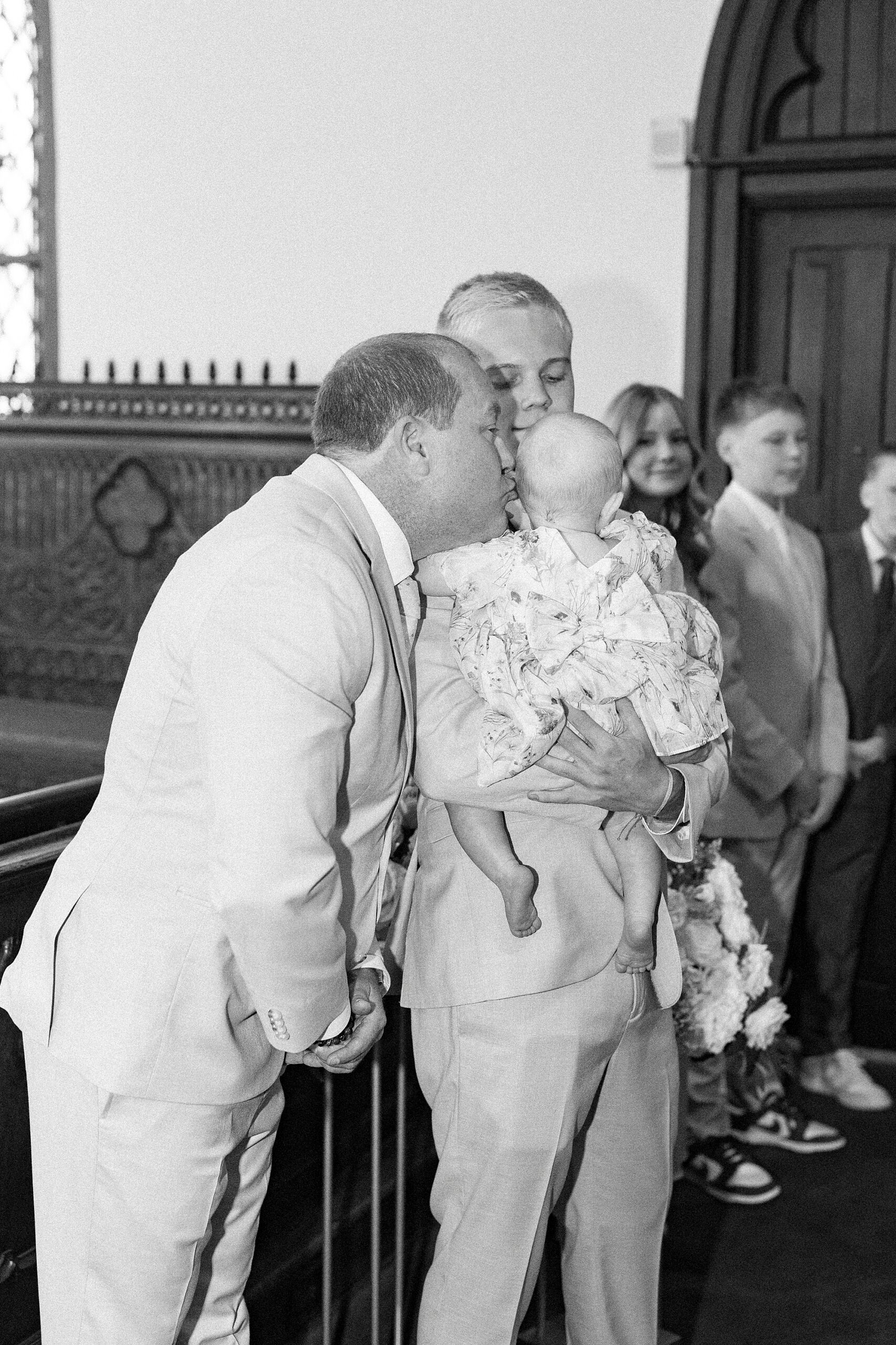 man leans to kiss daughter that son holds inside St. Mary's Chapel