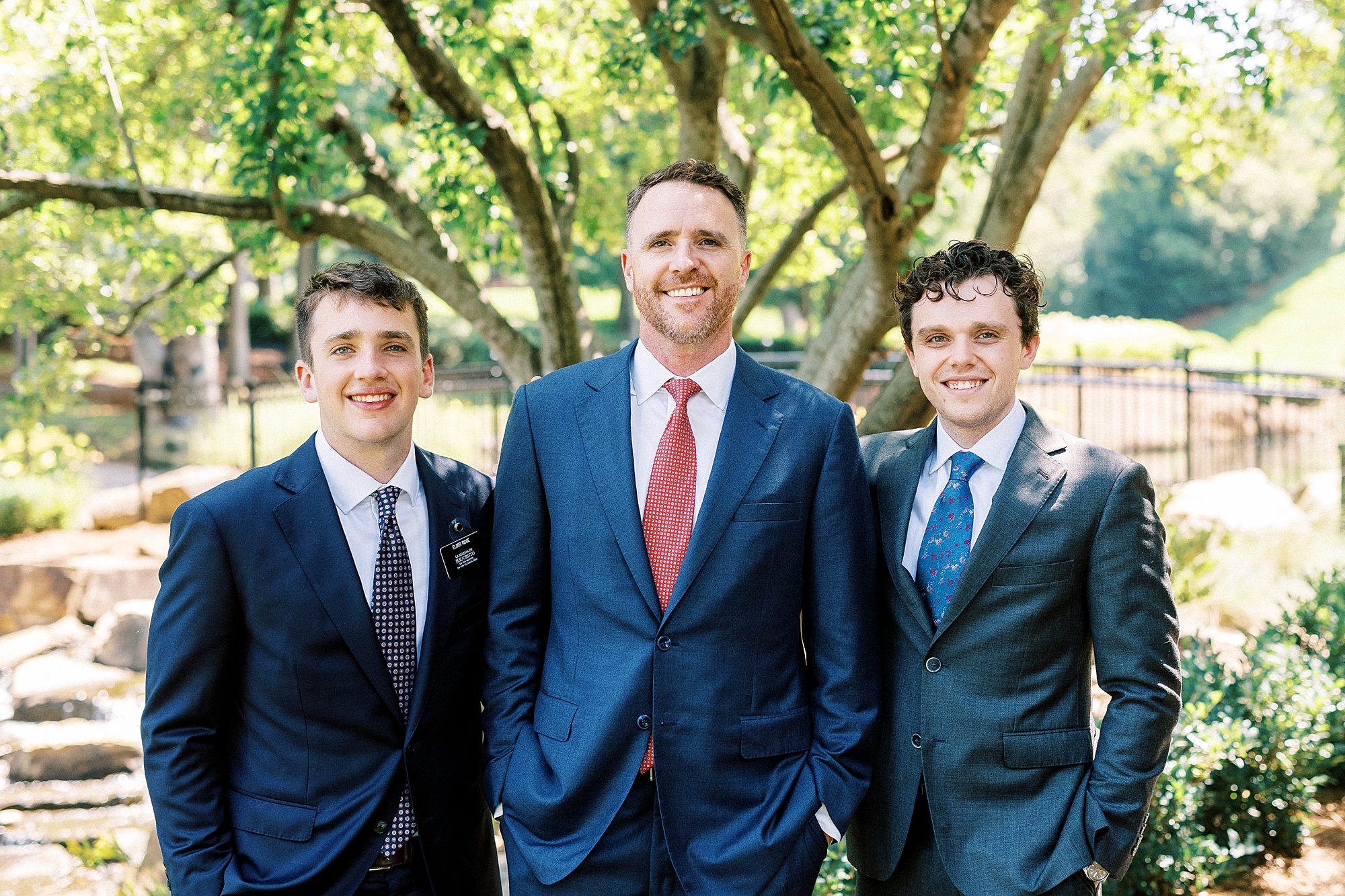 dad stands with two sons in suits in Cullman Park